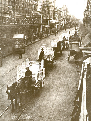 Old hospital beds being wheeled down a street.